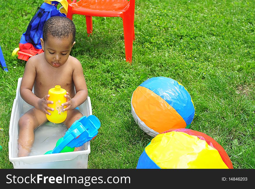 Young child playing outside in small pool of water with beechballs around. Young child playing outside in small pool of water with beechballs around