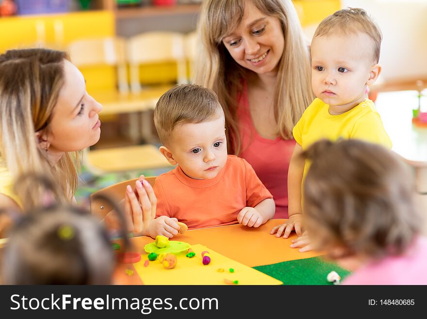 Babies with teachers play colorful clay toy in nursery