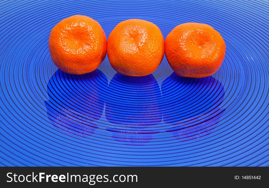 Three tangerines in row on blue glass plate