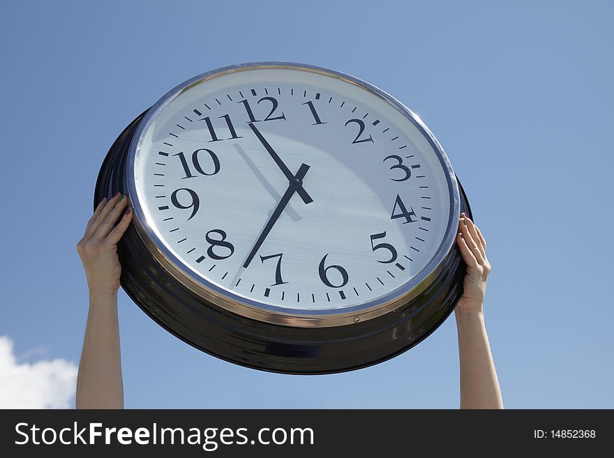 Hands lifting a big clock outdoors on a summer day. Blue sky background. Hands lifting a big clock outdoors on a summer day. Blue sky background.