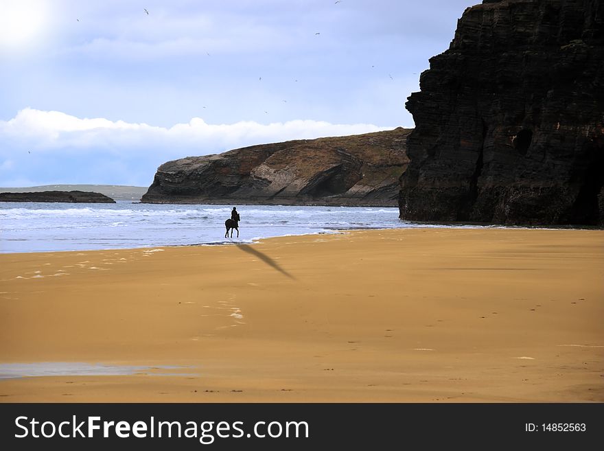 Silhouette of a horse and rider galloping on ballybunion beach with cliffs at sunset in kerry ireland. Silhouette of a horse and rider galloping on ballybunion beach with cliffs at sunset in kerry ireland