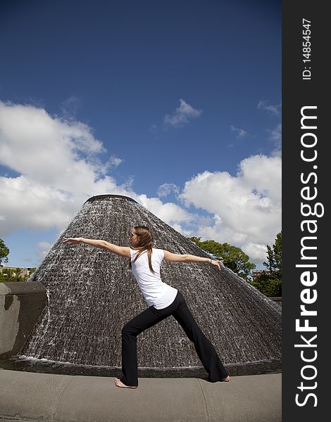 A woman doing her yoga stretch in a park in front of a water fountain with a blue sky. A woman doing her yoga stretch in a park in front of a water fountain with a blue sky.