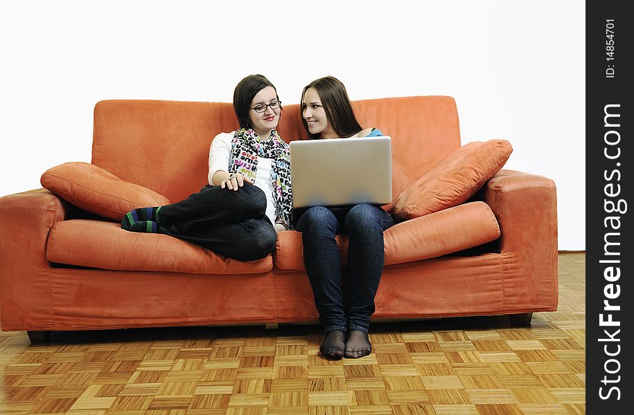 Two happy young woman working on laptop computer on red sofa isolated on white. Two happy young woman working on laptop computer on red sofa isolated on white