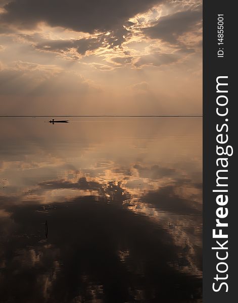 A silhoutte of a small boat on a dam water which reflected the light and rainy cloud. A silhoutte of a small boat on a dam water which reflected the light and rainy cloud