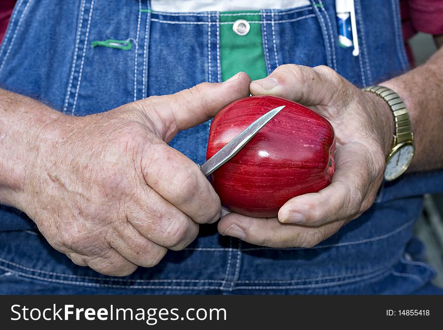 Old man in overalls about to peel a red apple. Old man in overalls about to peel a red apple