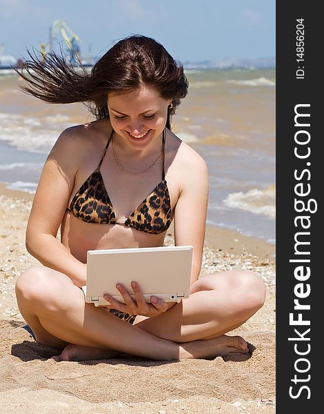 Happy young woman with a laptop sitting on the sand. Happy young woman with a laptop sitting on the sand