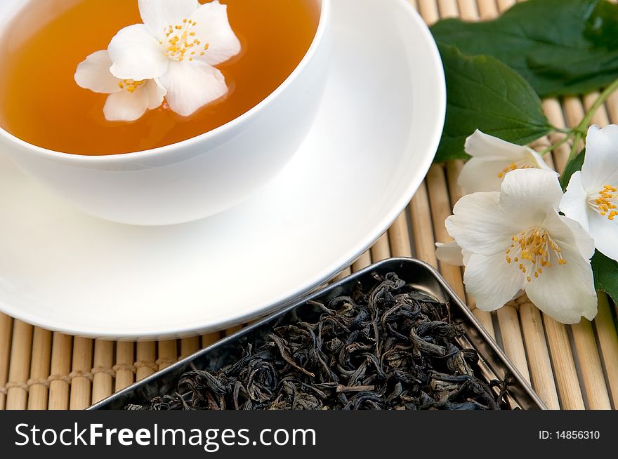 A cup of tea on a tray with dried tea and jasmine branch. A cup of tea on a tray with dried tea and jasmine branch