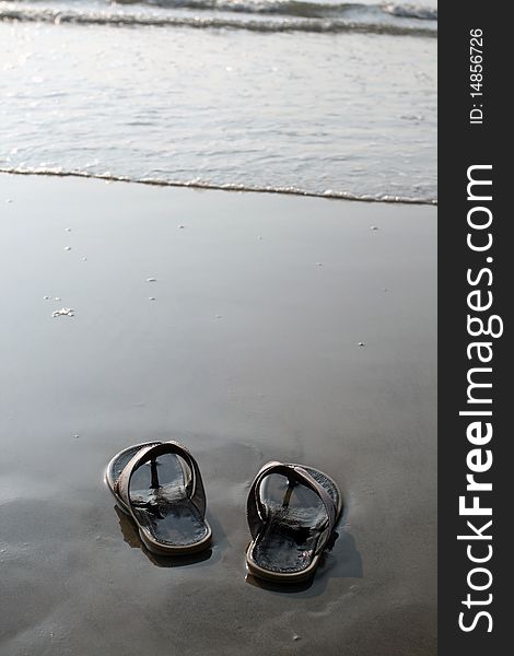 Black slippers standing on the wet sand near the water. Black slippers standing on the wet sand near the water