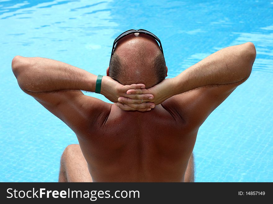 Man sitting near the pool and sunbathe, back