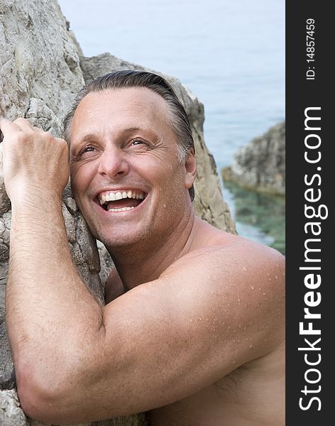 A color portrait photo of a happy mature man laughing as he leans against a rock at the beach. A color portrait photo of a happy mature man laughing as he leans against a rock at the beach.