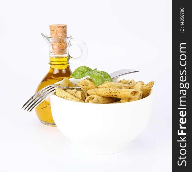 Penne with pesto decorated with basil and a fork in a bowl and a bottle of olive oil. Penne with pesto decorated with basil and a fork in a bowl and a bottle of olive oil