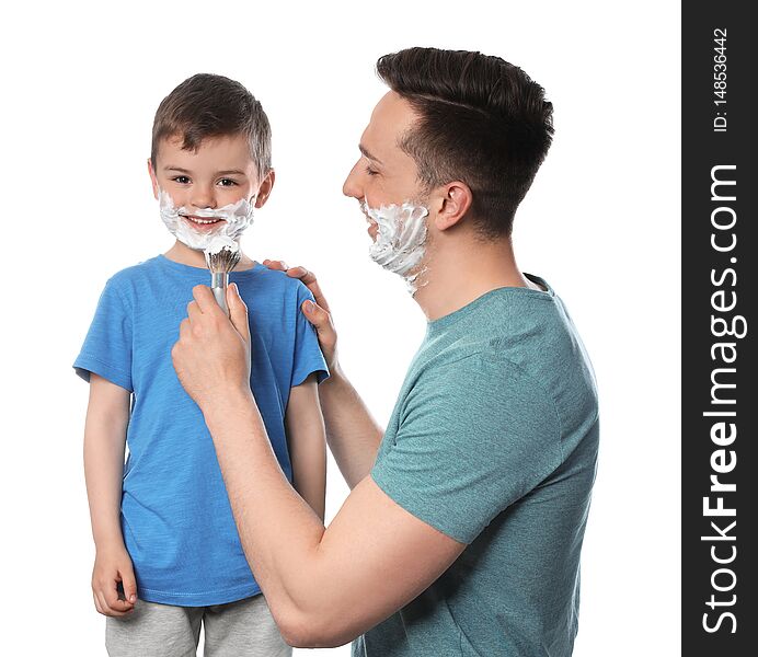 Dad applying shaving foam onto son`s face against white background