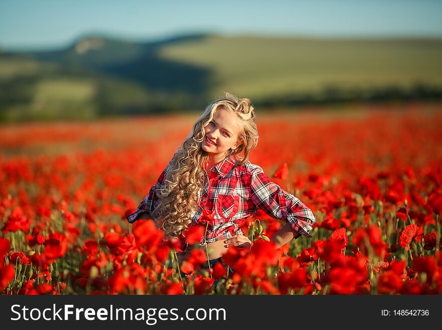 Young blonde in a red shirt in the poppy flower field.