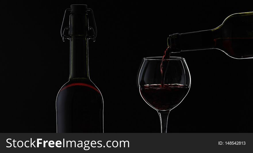 Wine. Red wine pouring in wine glass over black background. Rose wine pour from the bottle. Silhouette. Close up shot. Wine. Red wine pouring in wine glass over black background. Rose wine pour from the bottle. Silhouette. Close up shot