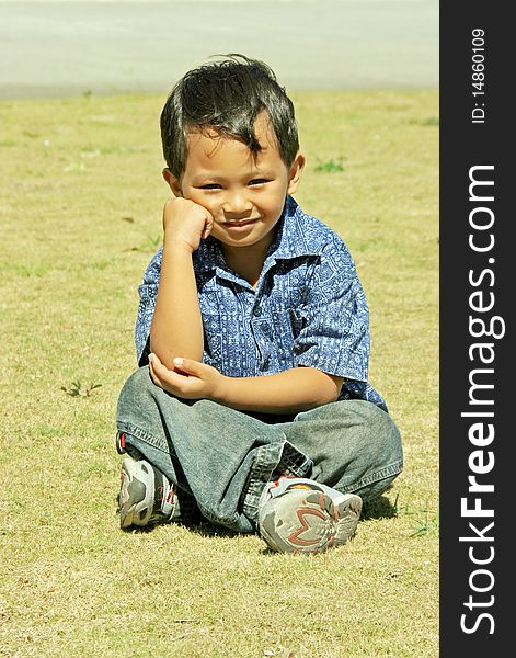 An Asian young boy setting in the grass land. An Asian young boy setting in the grass land