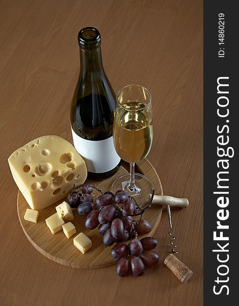 Bottle and glass of white wine with cheese, grapes, a cork and a corkscrew on a wood background