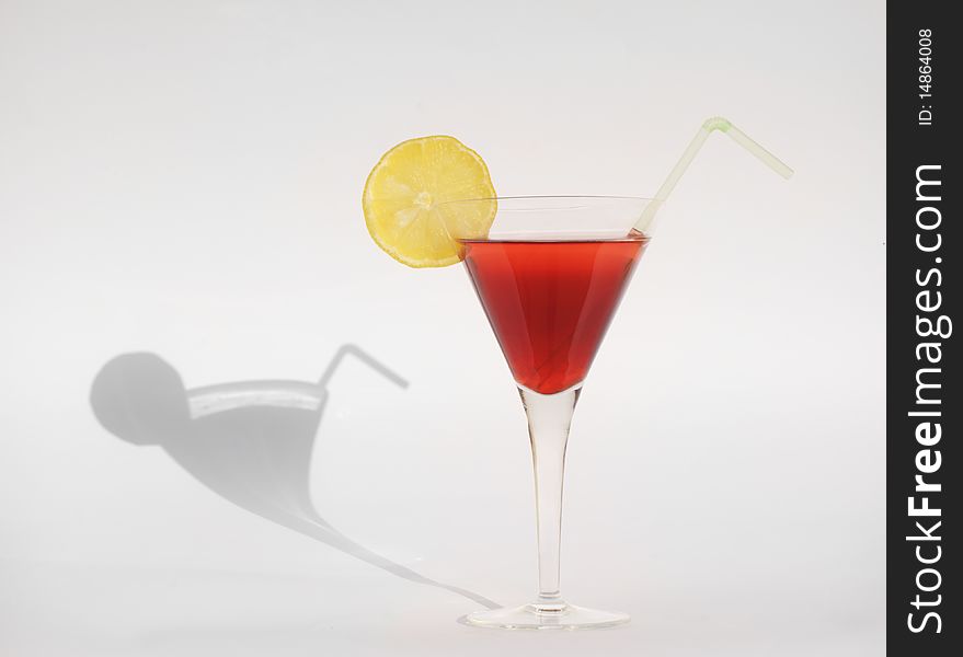 A red martini with a lemon and a straw and its shadow on sunny day. A red martini with a lemon and a straw and its shadow on sunny day