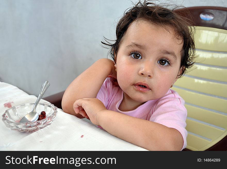 A little girl with lips dirty with jam sitting near an empty saucer. A little girl with lips dirty with jam sitting near an empty saucer