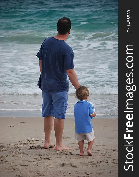 A father and son looking out at the ocean and the waves and they are both dressed in blue. A father and son looking out at the ocean and the waves and they are both dressed in blue.