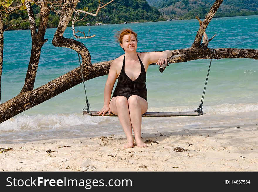 Happy woman sitting on a swing, relaxing on a idyllic beach like paradise