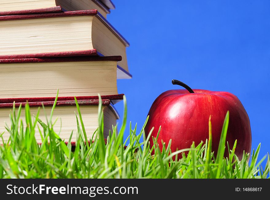 Red books and apple on a green grass. Red books and apple on a green grass.