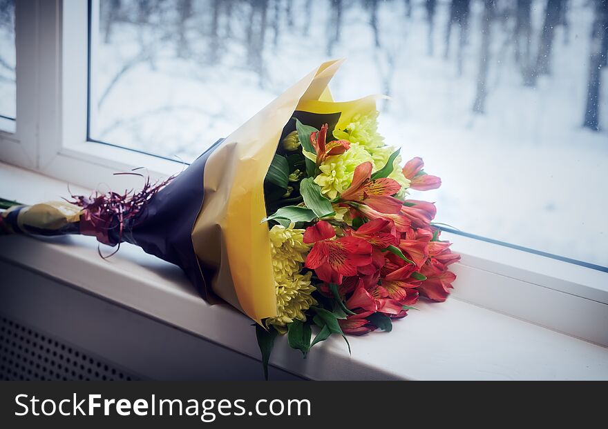 On the windowsill lies a beautifully packaged bouquet of fresh chrysanthemum and Amaryllis flowers. Outside the window winter landscape. On the windowsill lies a beautifully packaged bouquet of fresh chrysanthemum and Amaryllis flowers. Outside the window winter landscape