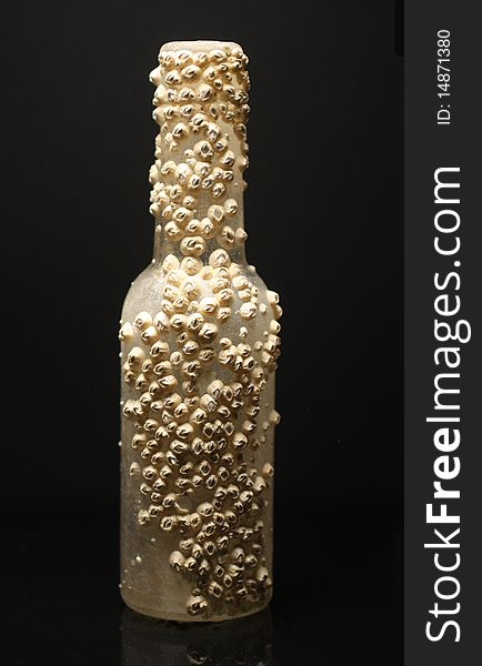 Bottle covered in barnacles against a black background. Bottle covered in barnacles against a black background.