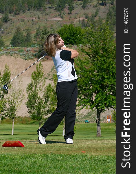 Blond female golfer following her ball from the tee-box