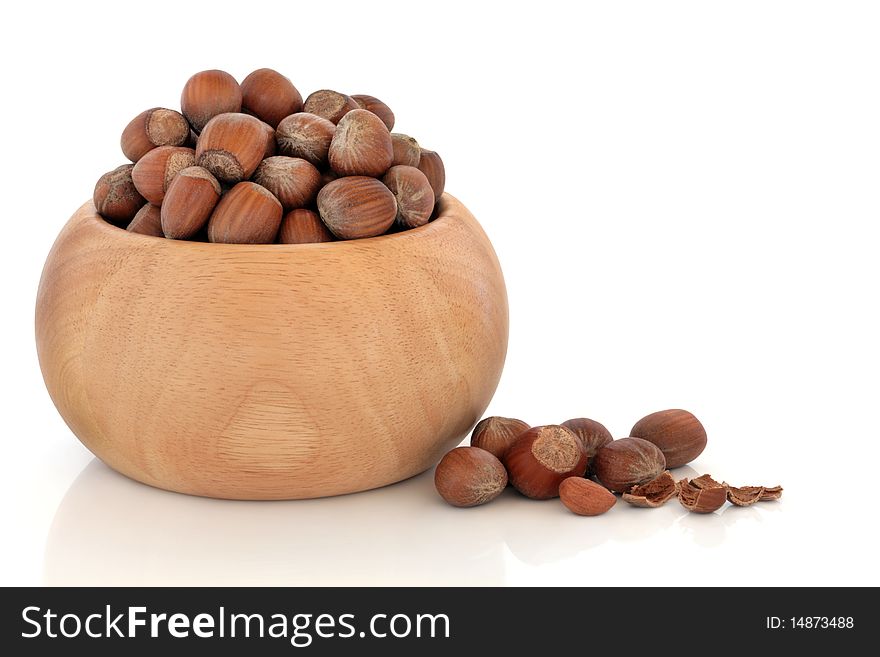 Hazelnuts in a beech wood bowl and scattered, isolated over white background with reflection.