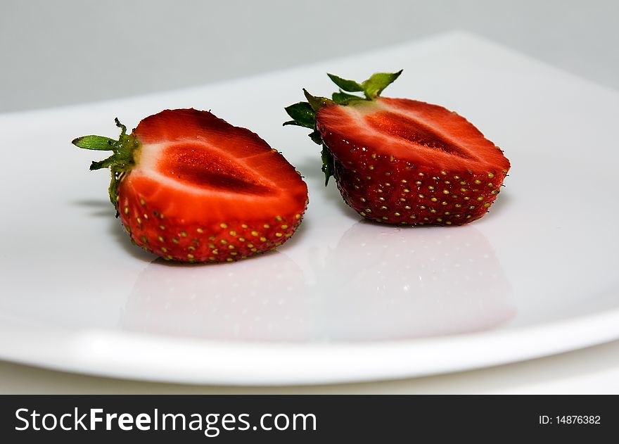 The mature red berry, cut on a half, (strawberry) on a white bowl. The mature red berry, cut on a half, (strawberry) on a white bowl