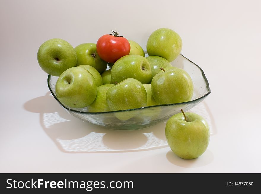 Green apples and one tomatoe in a glass vase