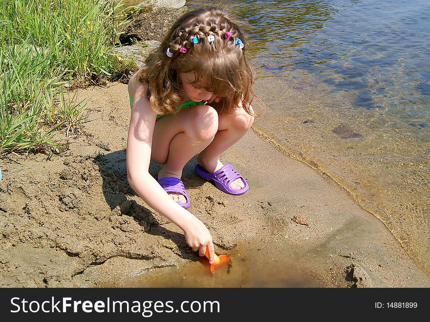 In the summer on the bank of lake the child plays sand at water. In the summer on the bank of lake the child plays sand at water