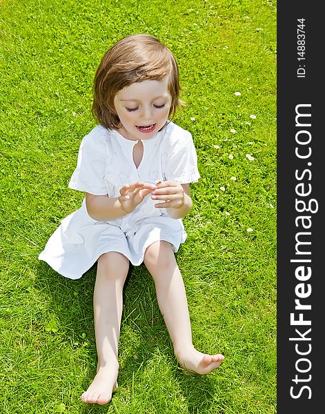 Three years old girl with daisy flower on garden grass