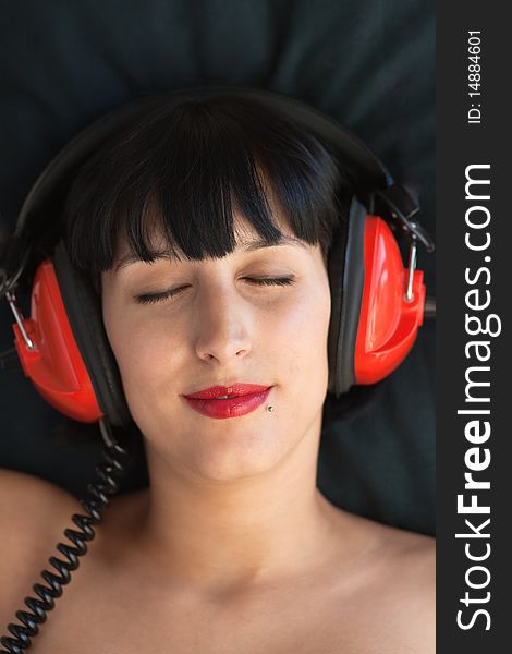 Beautiful women rests her head against a black pillow while enjoying music through her red head phones, relaxing. Beautiful women rests her head against a black pillow while enjoying music through her red head phones, relaxing.