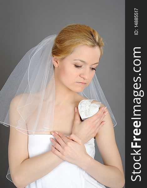 Beautiful young bride in white veil holding heart shaped engagement ring box. gray background. Beautiful young bride in white veil holding heart shaped engagement ring box. gray background