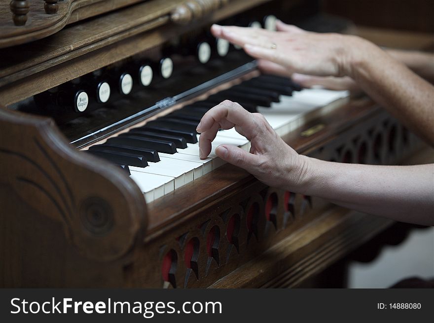This old wooden piano, is being played by mutipule hands. One hand, is touching the a white key. This old wooden piano, is being played by mutipule hands. One hand, is touching the a white key.