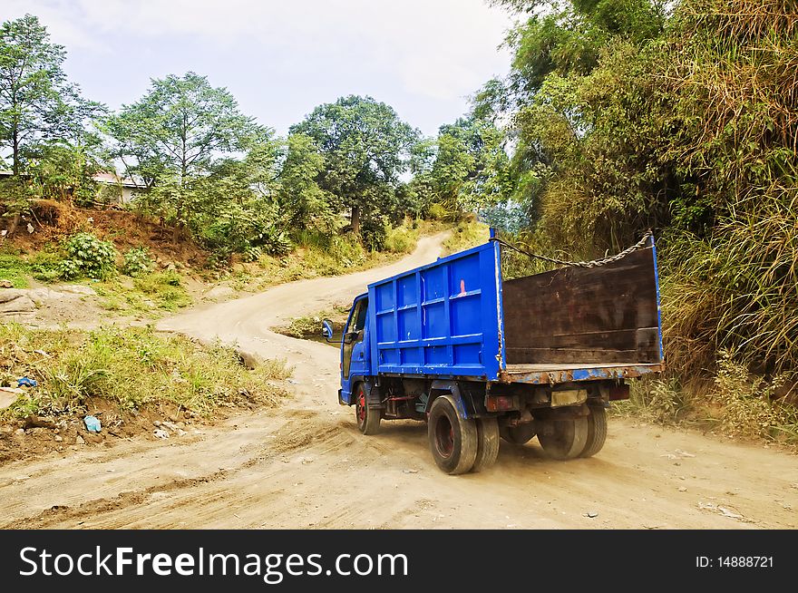 Empty, blue garbage truck on a winding rural dirt road