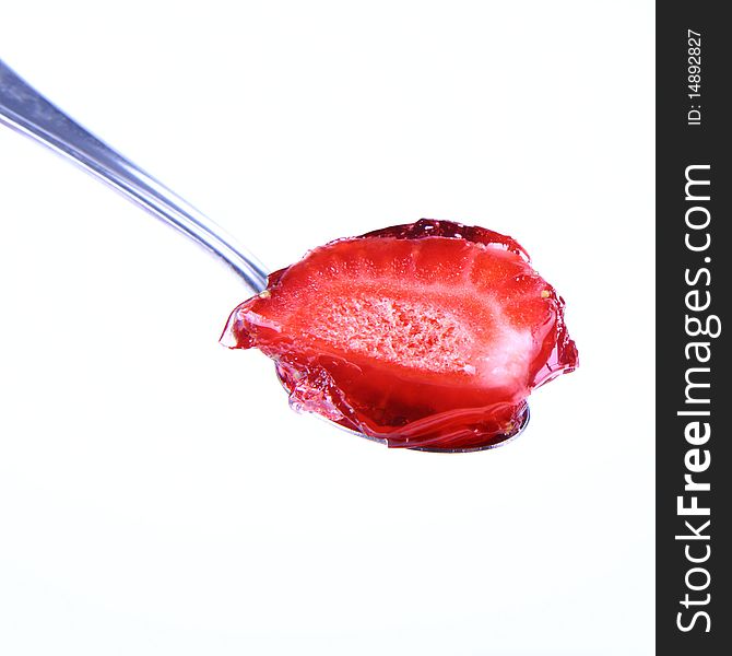 Piece of a strawberry covered with jelly on a spoon