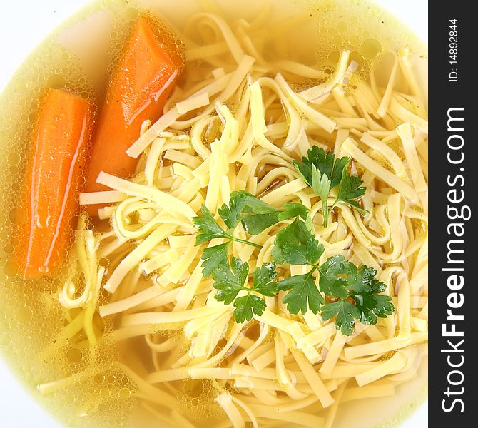 Chicken soup with macaroni and carrots decorated with parsley on a plate in close up