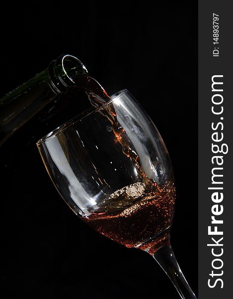 Photo of a glass and bottle pouring wine on black background, showing movement of the liquid. Photo of a glass and bottle pouring wine on black background, showing movement of the liquid