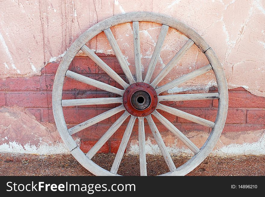 Old weathered wagon wheel leaning against brick wall. Old weathered wagon wheel leaning against brick wall