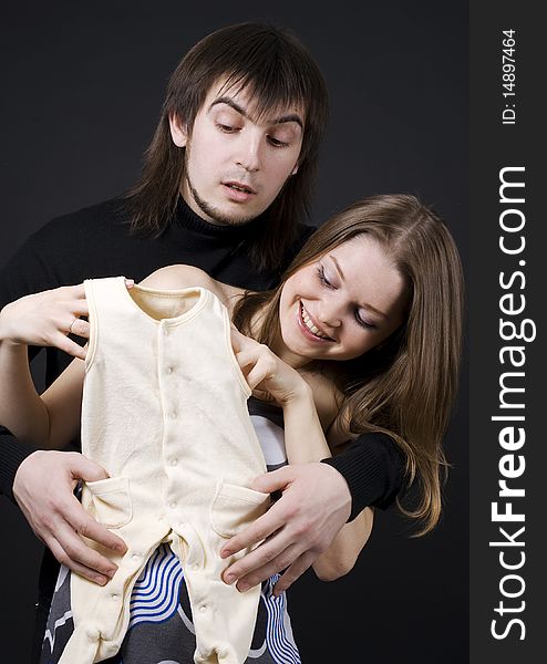 Pregnant couple embrace holding baby clothes. Pregnant couple embrace holding baby clothes