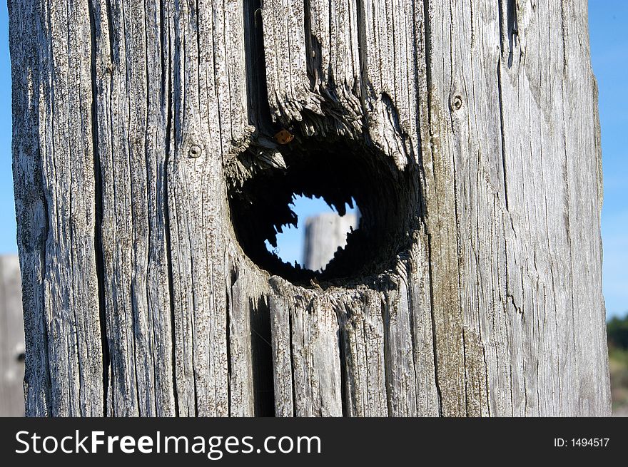 A wooden pole with a hole and another pole seen through it. A wooden pole with a hole and another pole seen through it.