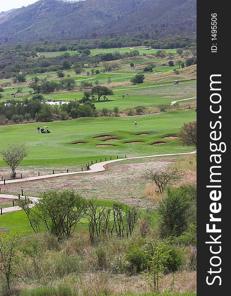 Golfers with a golf cart in the fairway surrounded by bunkers and hazards. Golfers with a golf cart in the fairway surrounded by bunkers and hazards