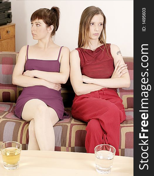 Two girls young women sitting on a sofa, looking opposite direction