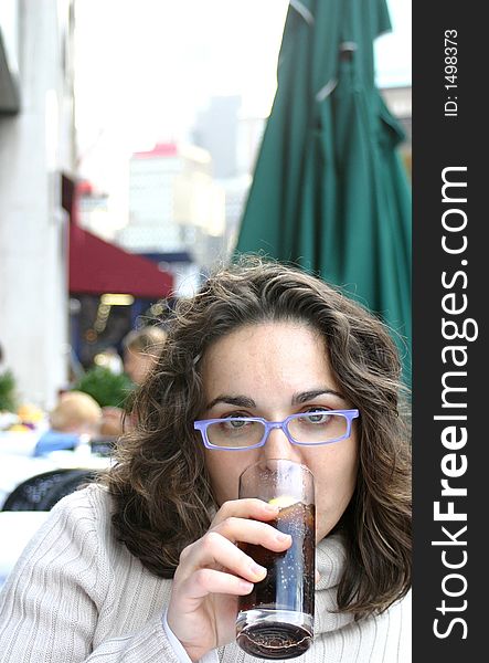 Attractive young woman in sidewalk city cafe, drinking a glass of cola. Attractive young woman in sidewalk city cafe, drinking a glass of cola.