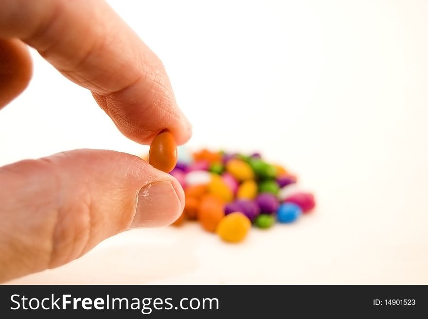 A man's hand holding a tiny piece of orange candy. A man's hand holding a tiny piece of orange candy