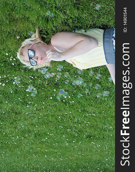 Young white Caucasian teenage girl laying in grass blowing bubbles with her sunglasses on, looking up at the sky. Young white Caucasian teenage girl laying in grass blowing bubbles with her sunglasses on, looking up at the sky.