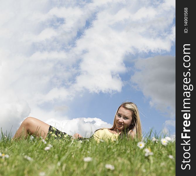 Closeup of a beautiful blond white Caucasian young adult teenage girl laying in a green grass field smiling at the camera with blue sky and white clouds above her for blank empty copyspace. Closeup of a beautiful blond white Caucasian young adult teenage girl laying in a green grass field smiling at the camera with blue sky and white clouds above her for blank empty copyspace.
