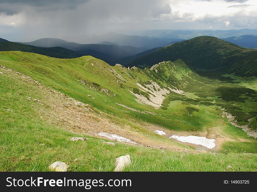 A summer hillside with snow in a landscape under white clouds